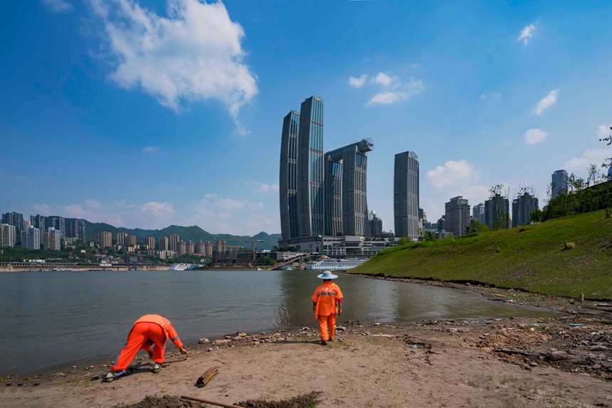 環衛工人冒著烈日清理河邊垃圾。黃進攝