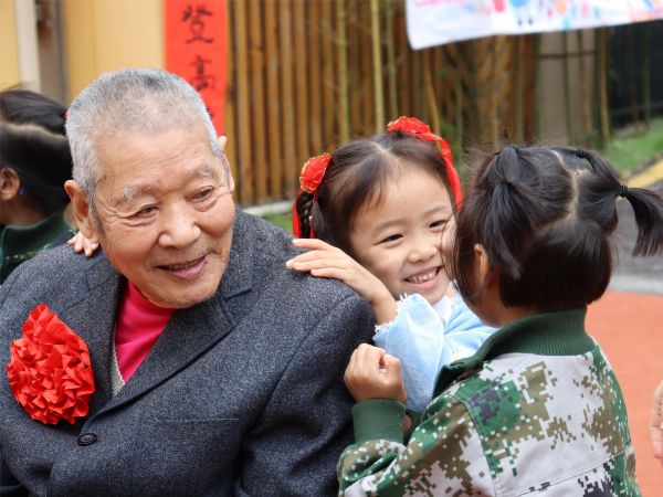兩位孩子正在為爺爺捶背。新絲路幼兒園供圖